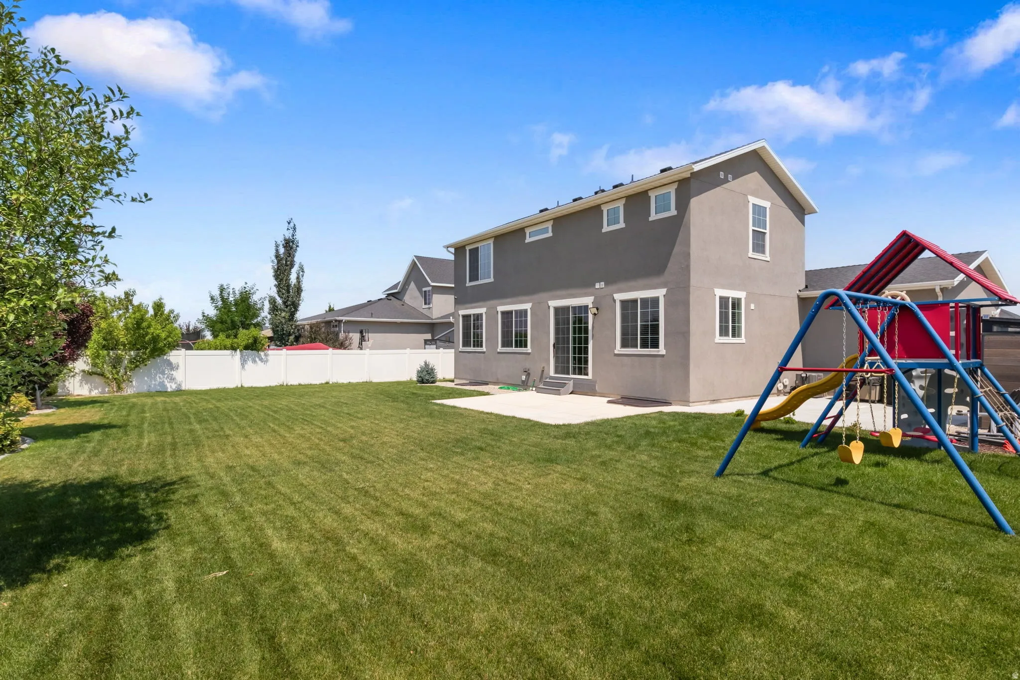 Expansive backyard featuring a manicured lawn, a white privacy fence, and a concrete patio