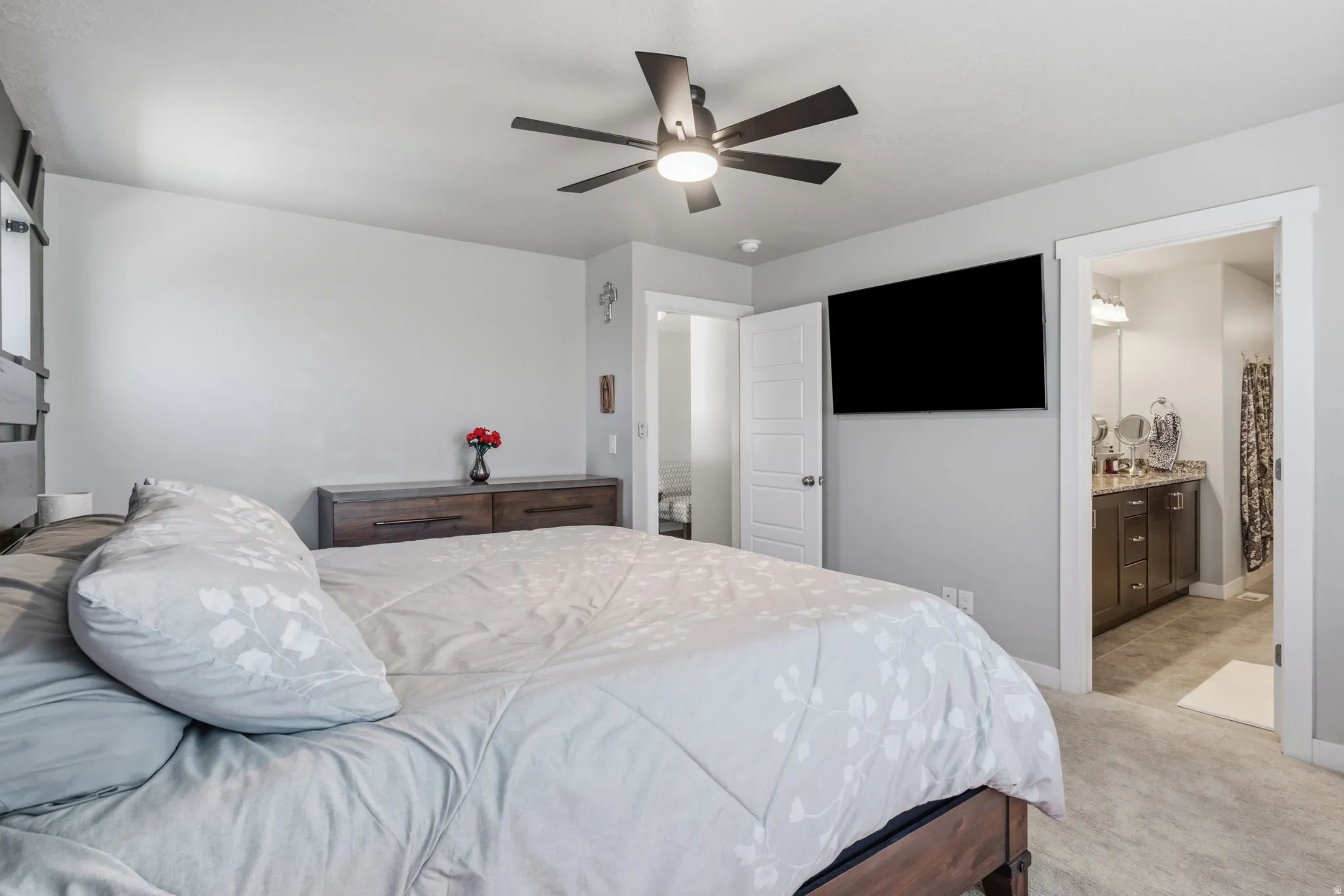 Carpeted bedroom with a ceiling fan, wall-mounted television, and a wood-finish dresser