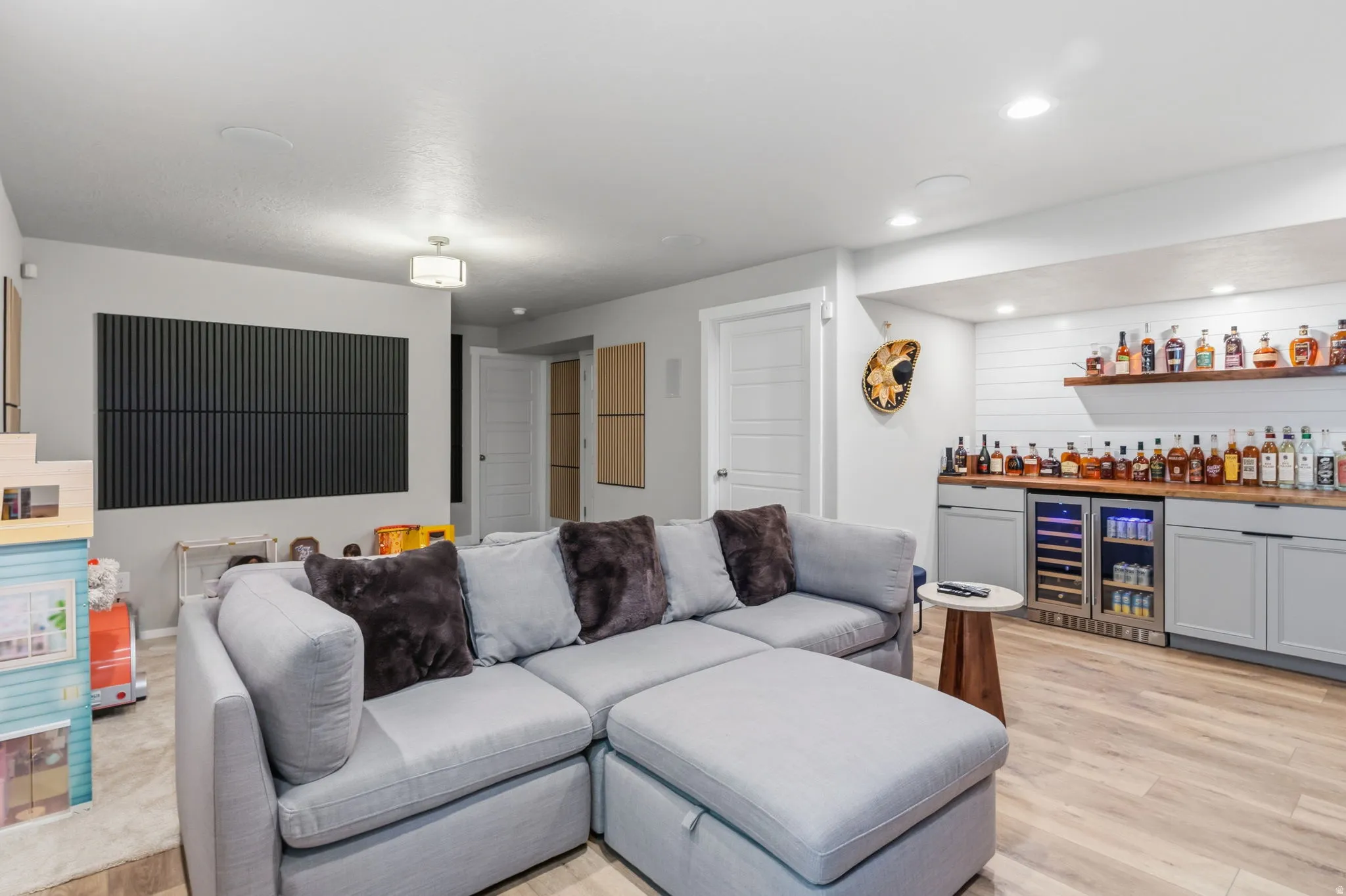 Dedicated entertainment area featuring light wood-finish flooring, recessed lighting, built-in cabinetry, and integrated beverage refrigerators