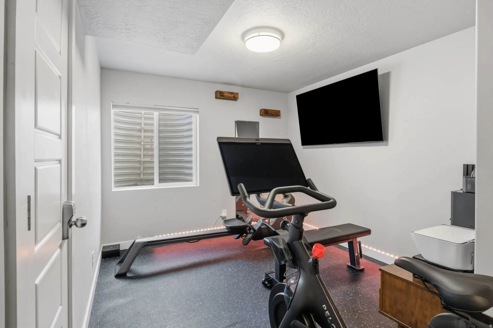Recessed window with horizontal blinds, wall-mounted television, and rubberized flooring