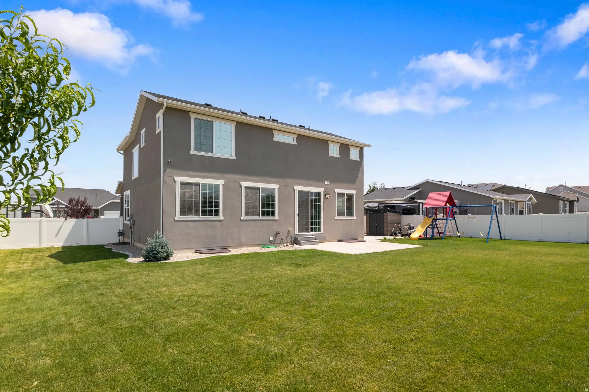 Spacious rear yard with a concrete patio, privacy fencing, and mature landscaping