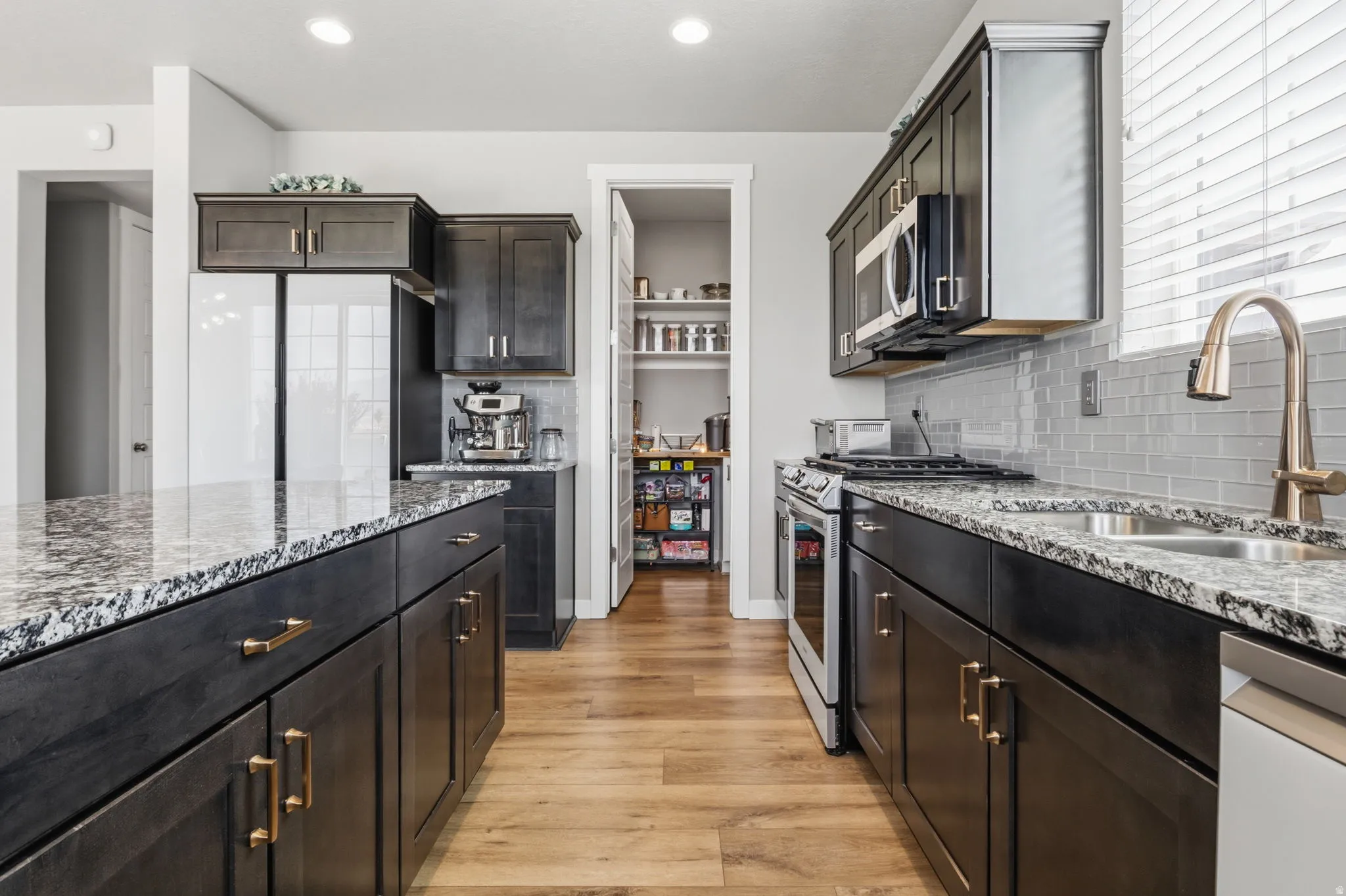 Kitchen featuring dark wood cabinetry, granite-style countertops, stainless steel appliances, a tile backsplash, and wood-finish flooring