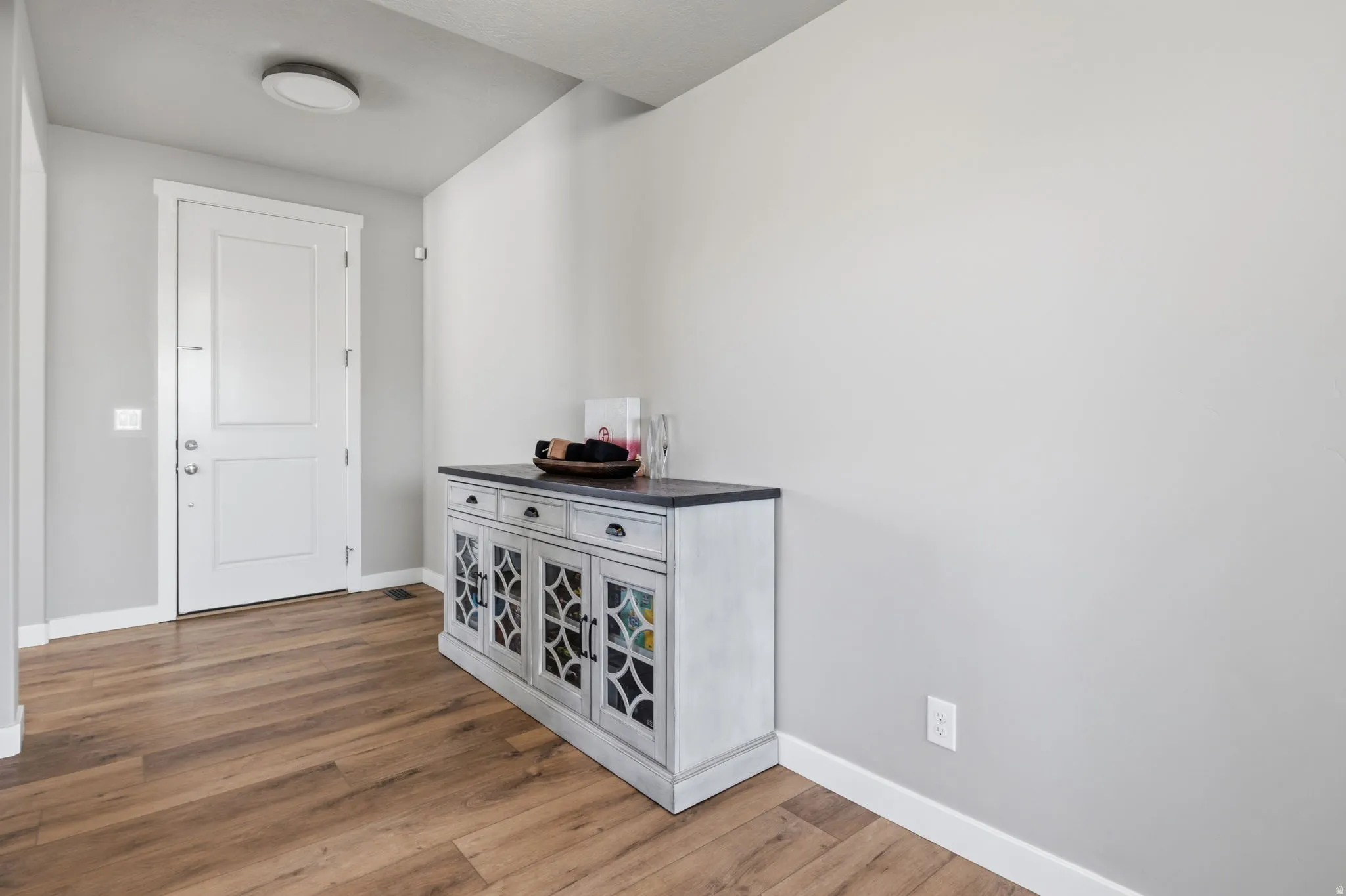 Wood-finish flooring, white entry door, recessed ceiling light, and light gray wall paint