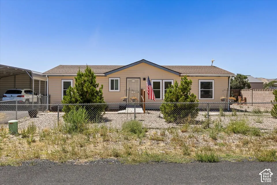 Siding exterior with a covered carport, chain-link fencing, and a gravel front yard