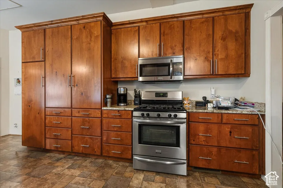 Wood cabinetry with crown molding, stainless steel appliances, stainless steel range with overhead microwave, and stone countertops