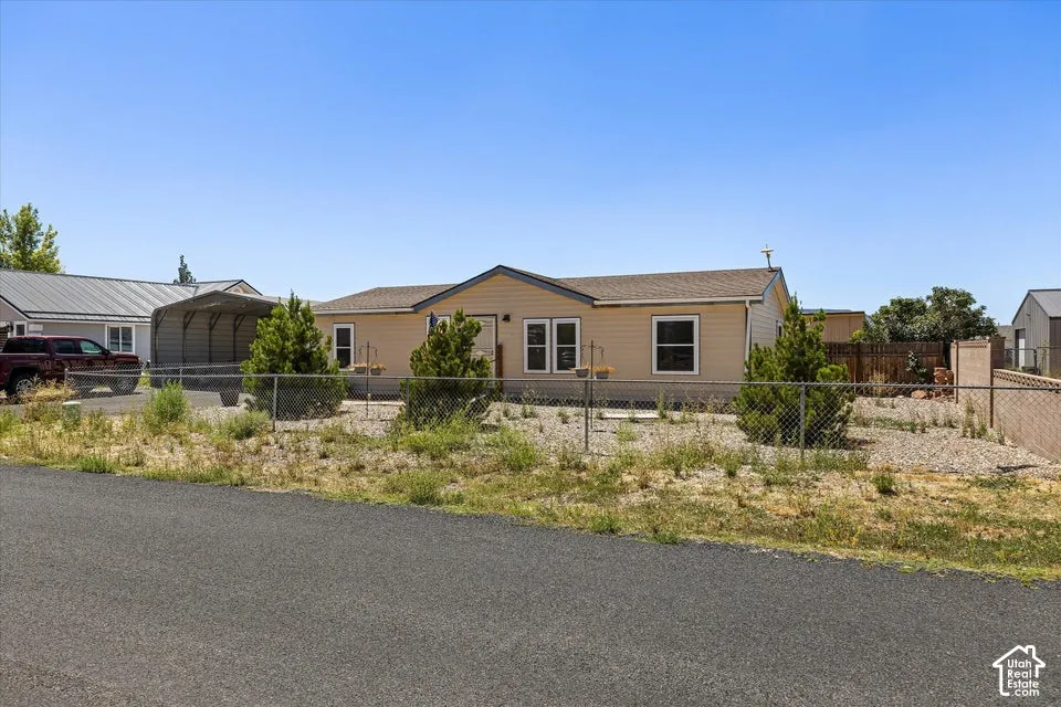 Single-story residence featuring light-colored siding, a chain-link fence, a paved driveway, and established landscape plantings
