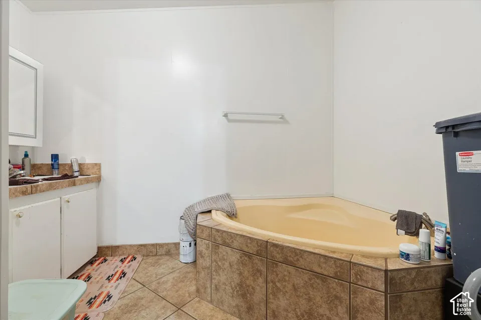 Corner soaking tub with tiled surround, single vanity with countertop, wood-finish flooring, and white walls