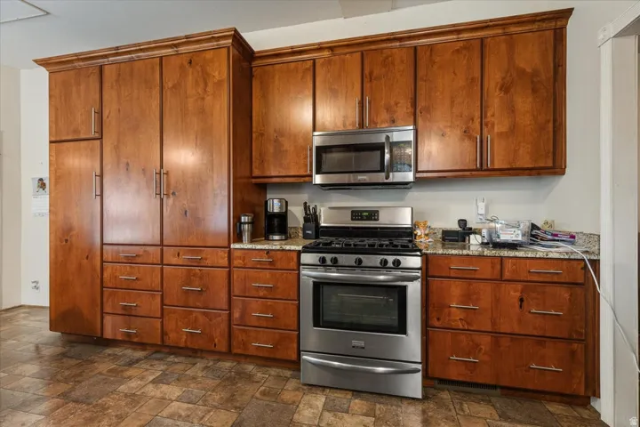 Wood cabinetry with crown molding, stainless steel appliances, stainless steel range with overhead microwave, and stone countertops