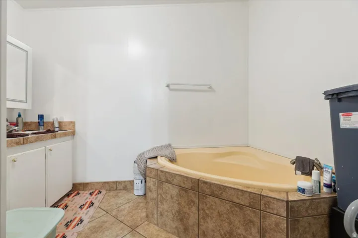 Corner soaking tub with tiled surround, single vanity with countertop, wood-finish flooring, and white walls