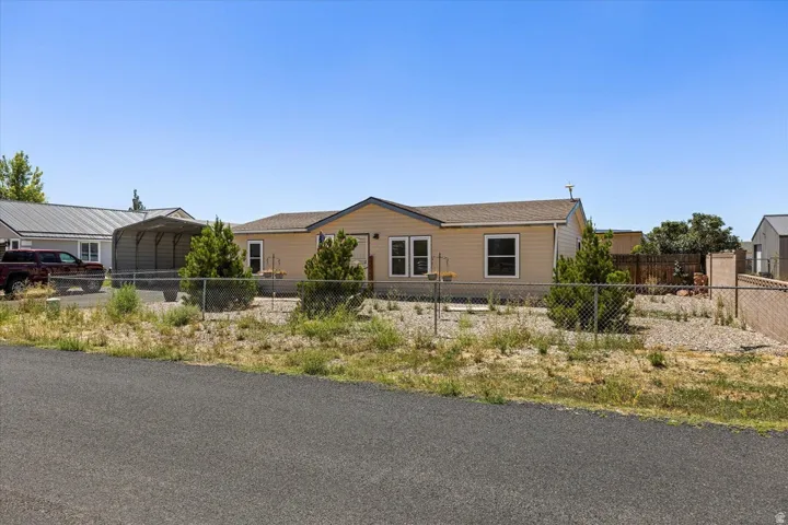 Single-story residence featuring light-colored siding, a chain-link fence, a paved driveway, and established landscape plantings