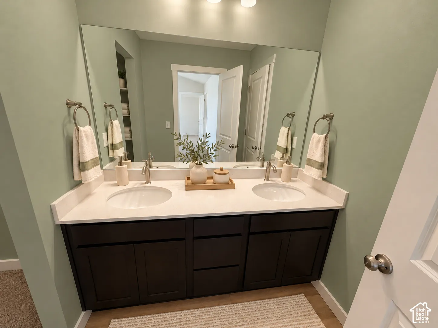 Double vanity featuring a light-toned countertop with dual integrated sinks, dark wood cabinetry, and a full-width mirror with wall-mounted metallic fixtures