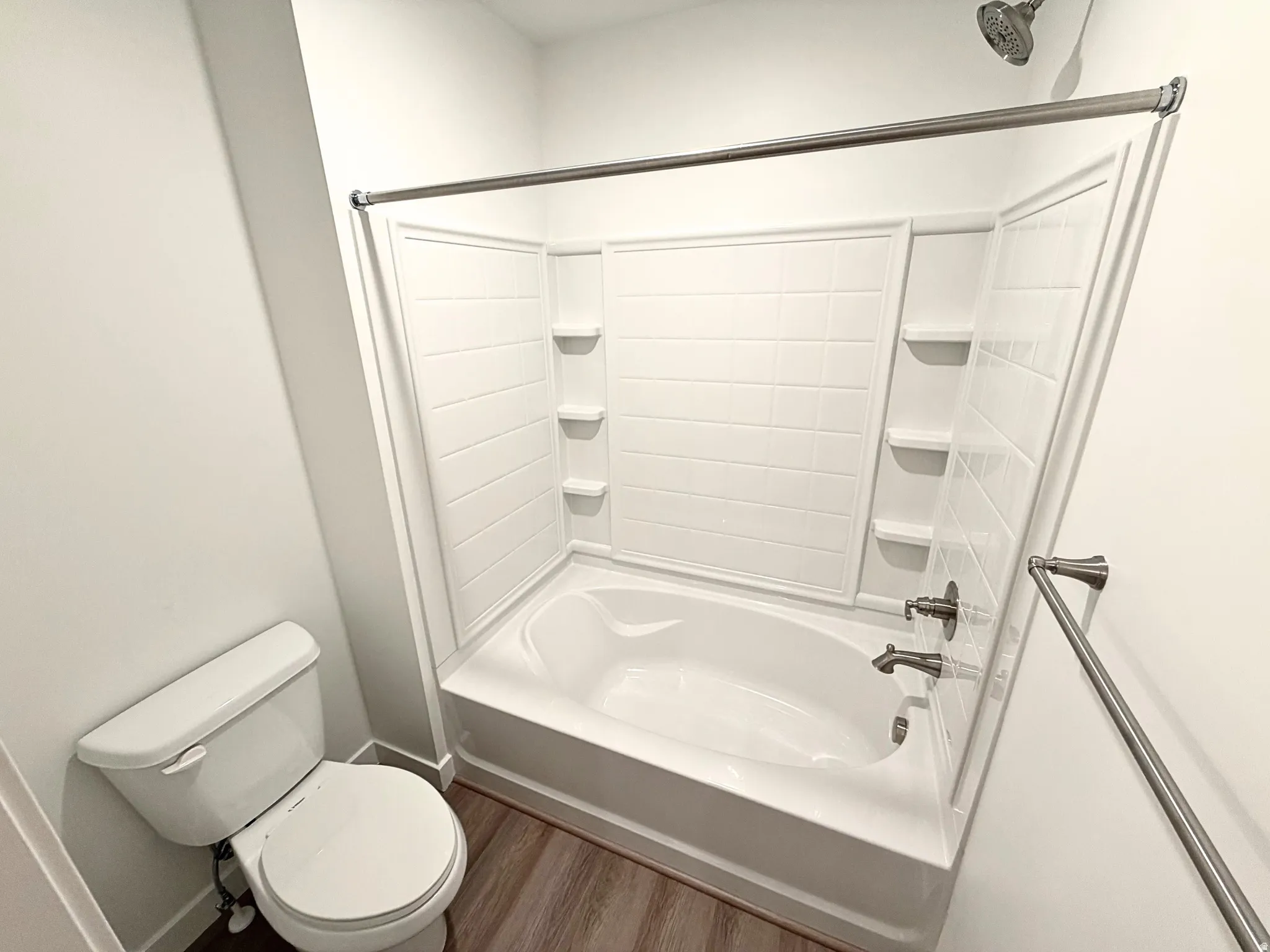 Tub and shower combination with integrated shelving, brushed nickel fixtures, and wood-finish flooring