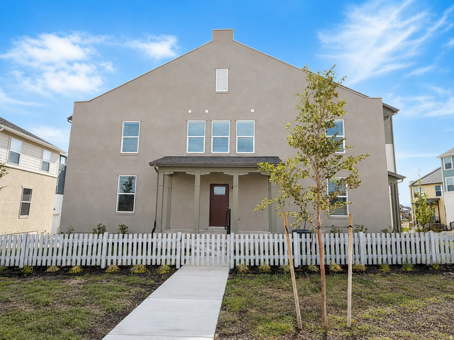 Stucco exterior with multiple windows, covered entry, and a front yard with a white picket fence