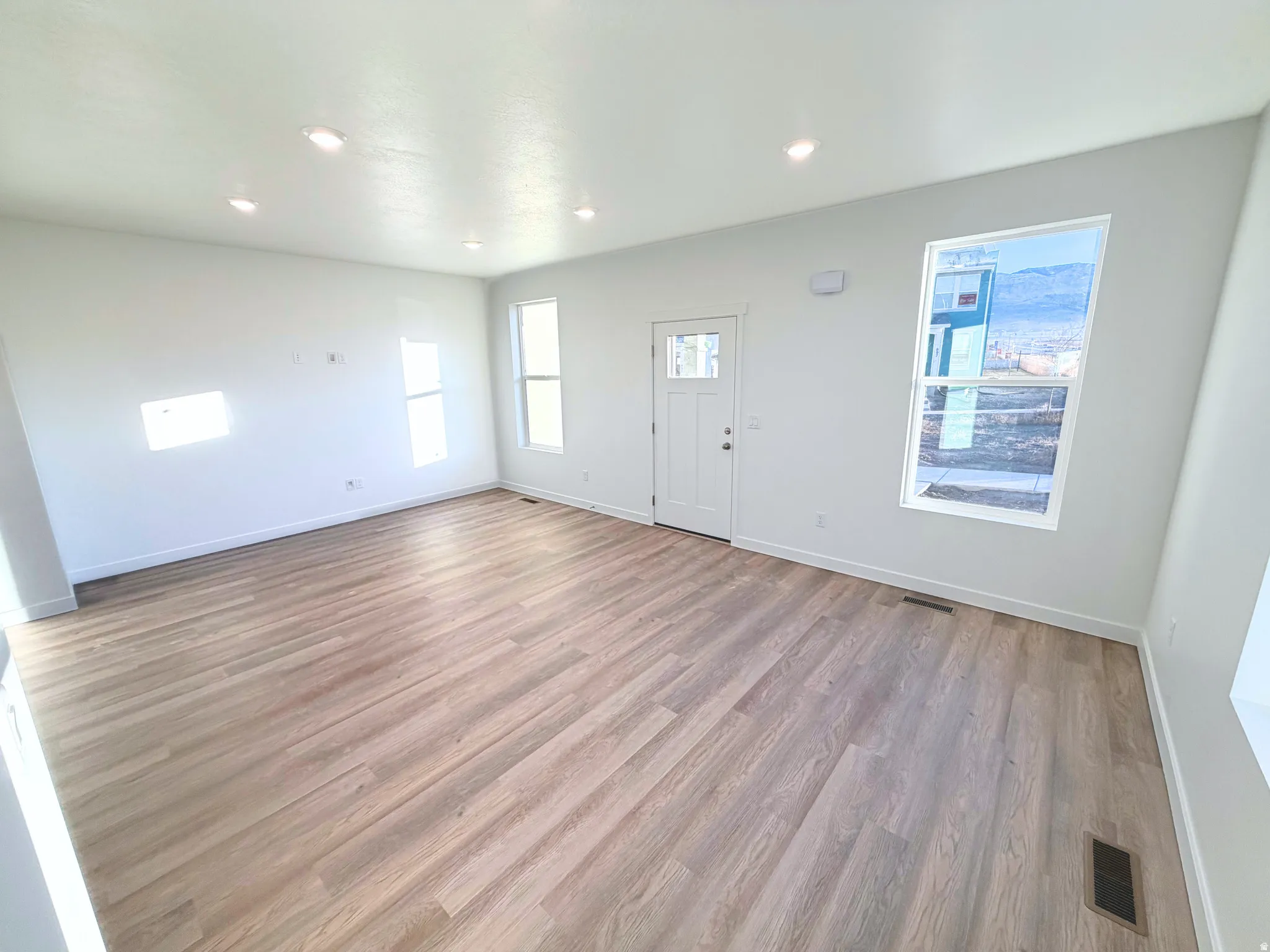 Open-concept living area featuring wood-finish flooring, recessed ceiling lighting, multiple windows, and a panel door with an integrated window