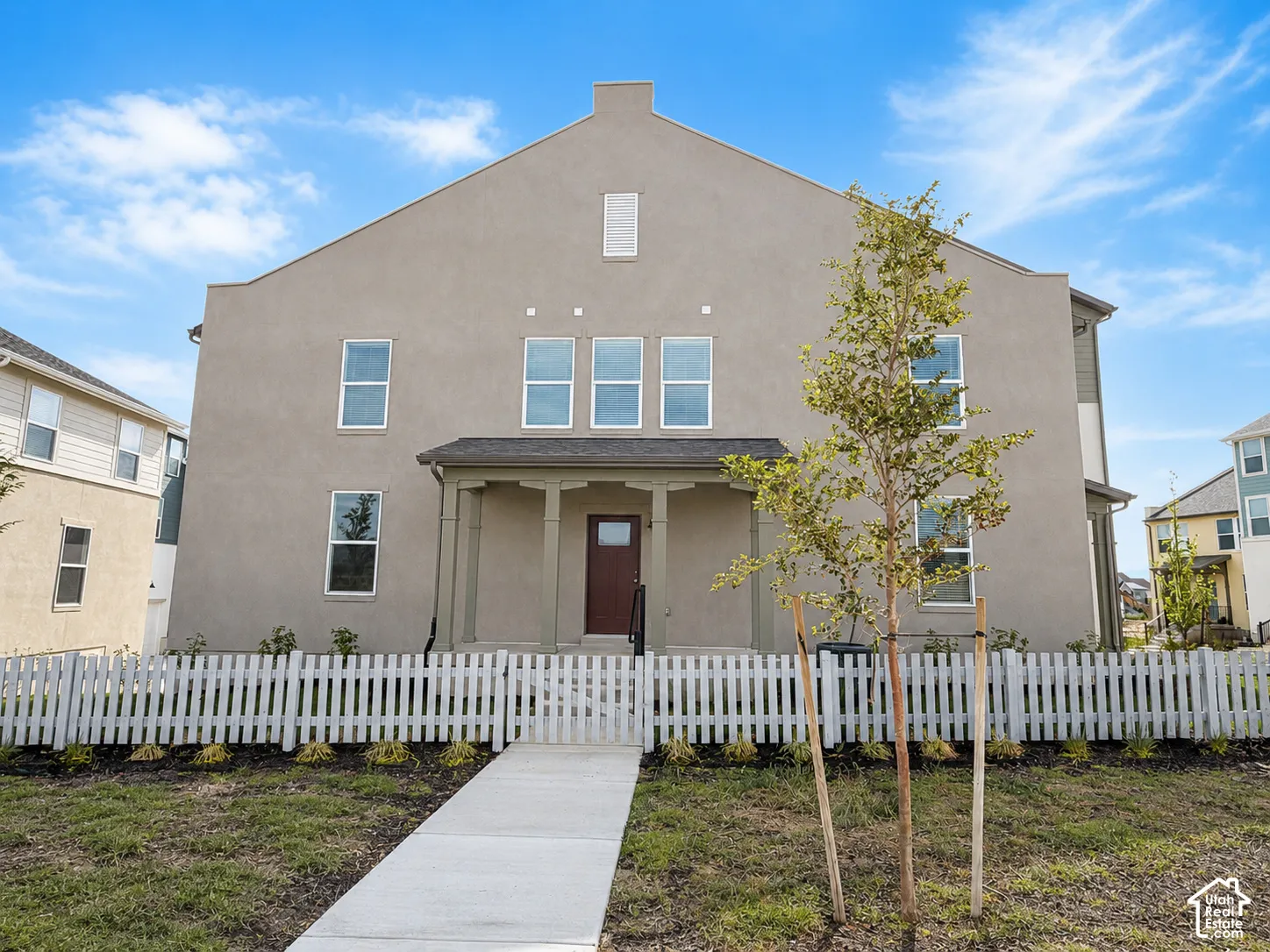 Stucco exterior with multiple windows, covered entry, and a front yard with a white picket fence