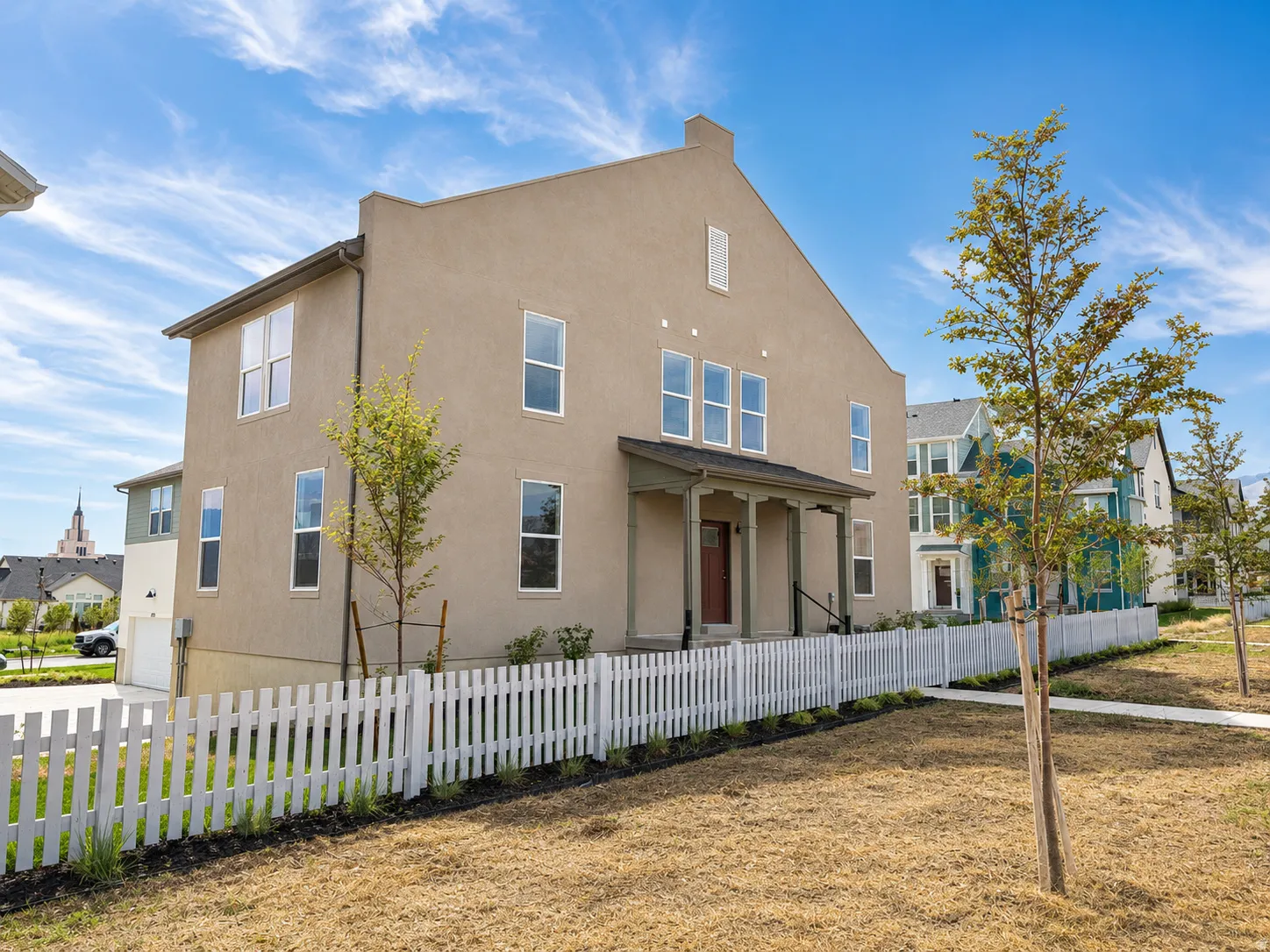 Stucco exterior with multiple windows, covered front porch, white picket fence, and attached garage