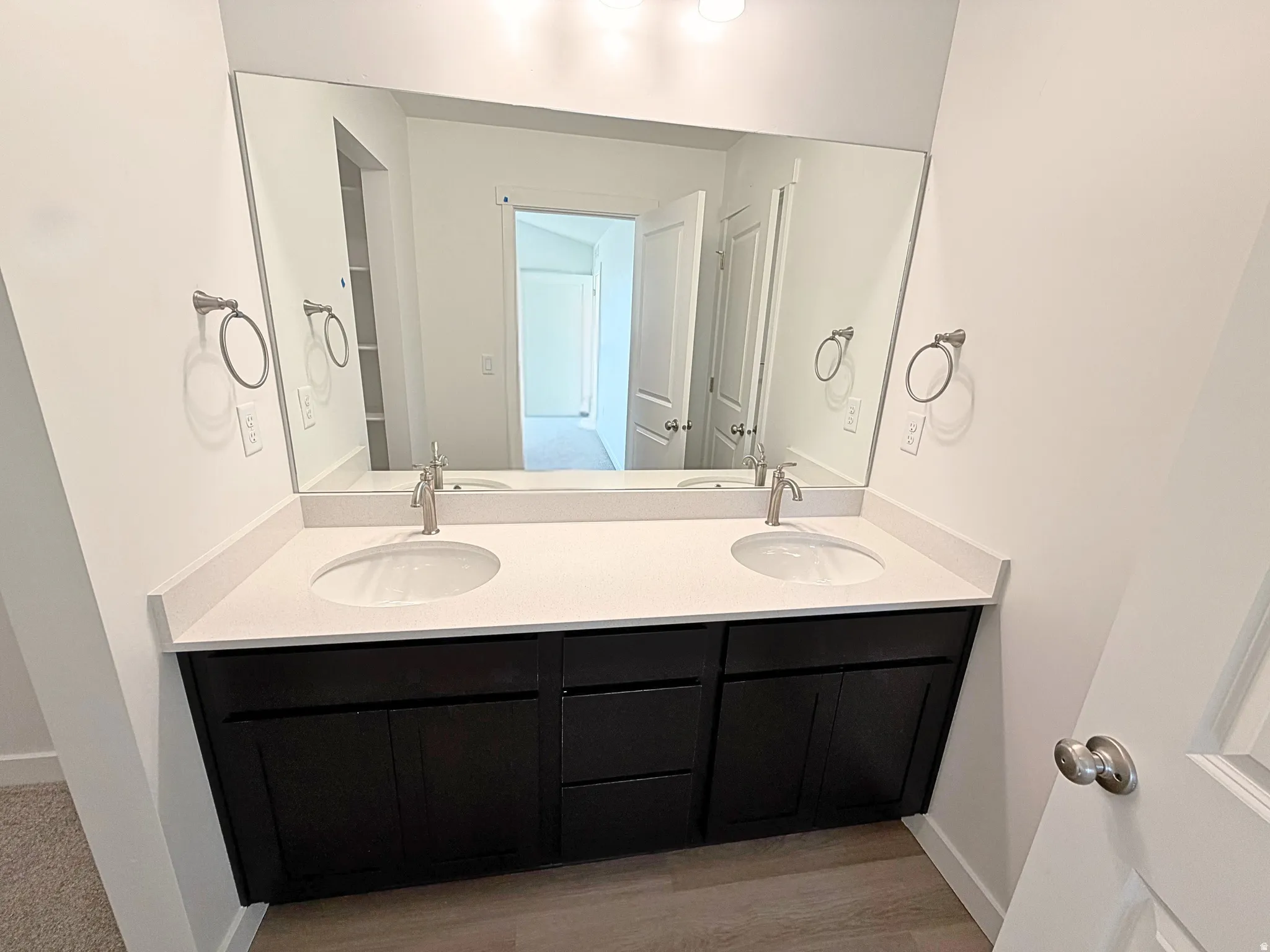 Dual under-mount sinks with brushed nickel faucets, dark wood-finish cabinetry, light-toned countertop, and a large wall-mounted mirror