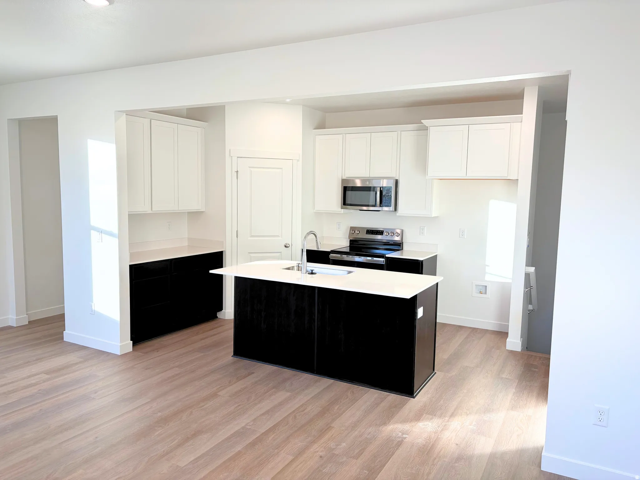 Open-concept kitchen with a central island, stainless steel appliances, two-tone cabinetry, and wood-finish flooring