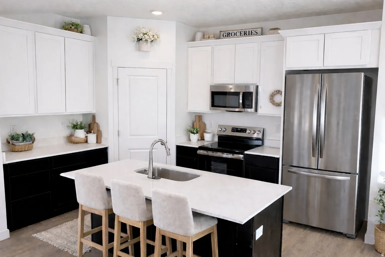 Kitchen featuring a central island with an undermount sink, two-tone cabinetry with white upper and black lower units, stainless steel appliances, and light-toned countertops