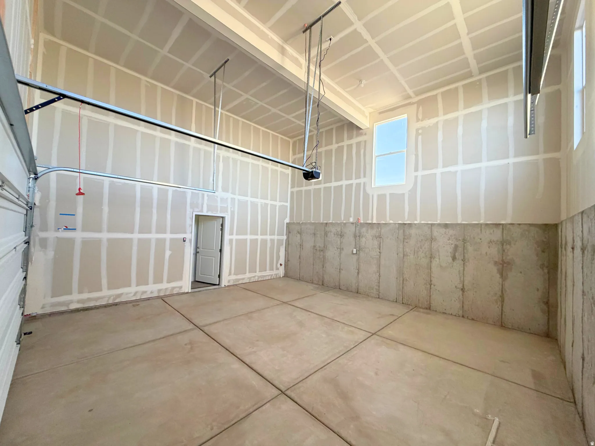 Spacious garage with high ceilings, unfinished drywall, concrete flooring, and multiple windows for natural light