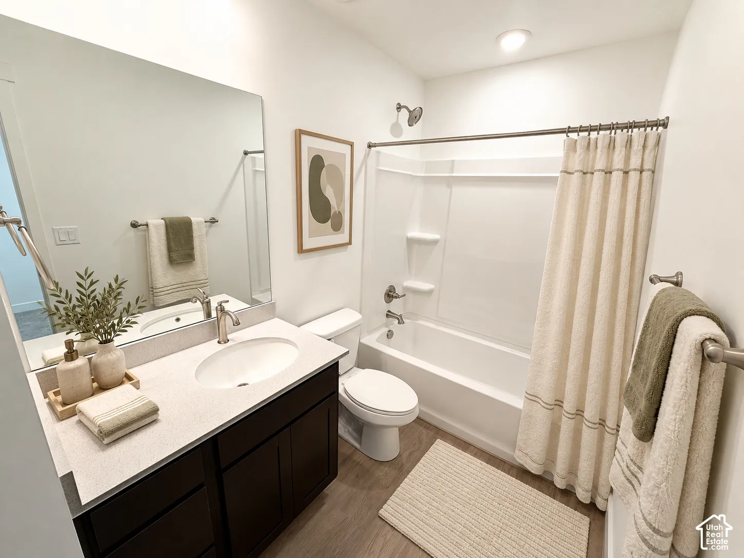 Bathroom featuring a vanity with a light-toned countertop, an undermount sink, a large wall-mounted mirror, a tub-shower combination with integrated shelving, and wood-finish flooring