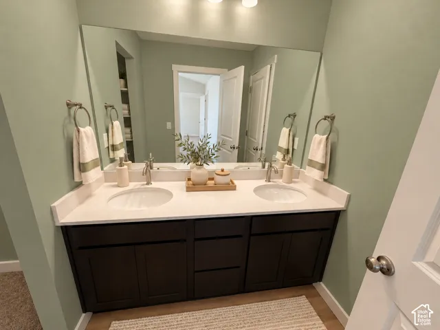 Double vanity featuring a light-toned countertop with dual integrated sinks, dark wood cabinetry, and a full-width mirror with wall-mounted metallic fixtures