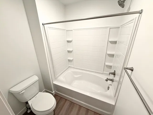 Tub and shower combination with integrated shelving, brushed nickel fixtures, and wood-finish flooring
