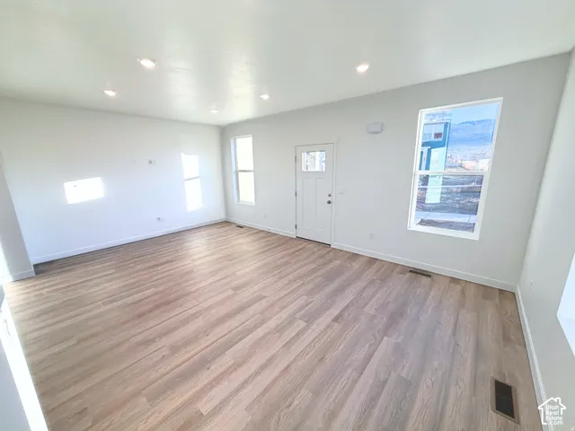 Open-concept living area featuring wood-finish flooring, recessed ceiling lighting, multiple windows, and a panel door with an integrated window