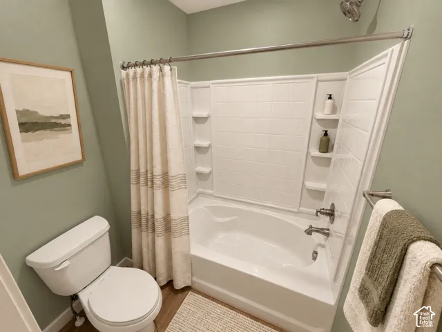Bathroom featuring a white molded tub-and-shower surround with integrated shelving, metallic finish showerhead and faucet, and wood-finish flooring