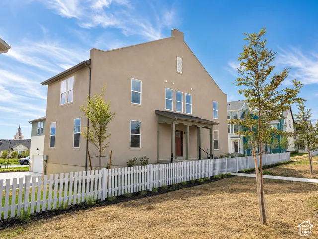Stucco exterior with multiple windows, covered front porch, white picket fence, and attached garage