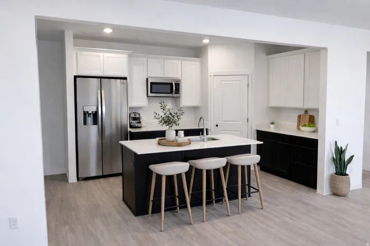 Kitchen featuring a central island with countertop, stainless steel appliances, white upper cabinetry, and black lower cabinetry