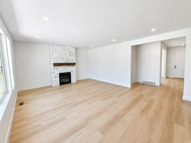 Open living space featuring wood-finish flooring, a stone-clad fireplace with a wood mantel, recessed lighting, and large windows