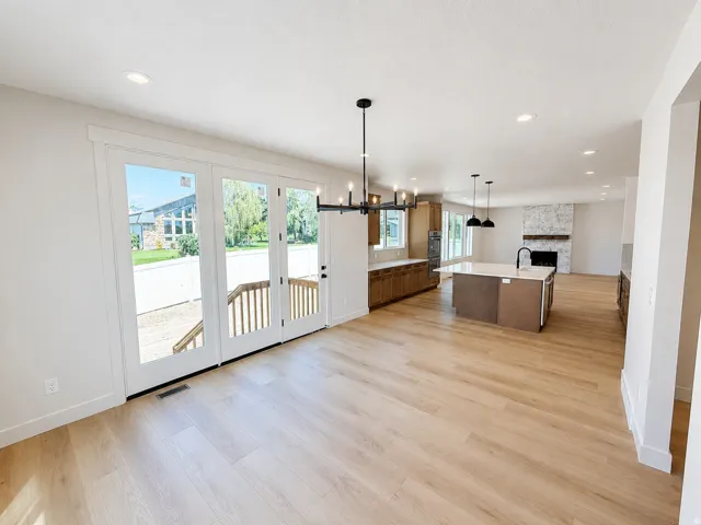 Open concept living space featuring wood-finish flooring, a kitchen island with seating, dark wood cabinetry, a fireplace with a stone surround, and recessed lighting