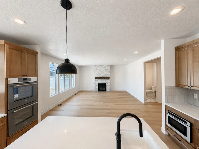 Modern kitchen with wood-finish cabinetry, integrated double ovens, white countertops, and a black pendant light