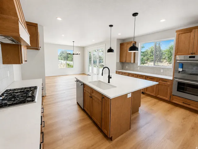 Kitchen featuring wood-finish cabinetry, white countertops, a gas cooktop, double wall ovens, and pendant lighting