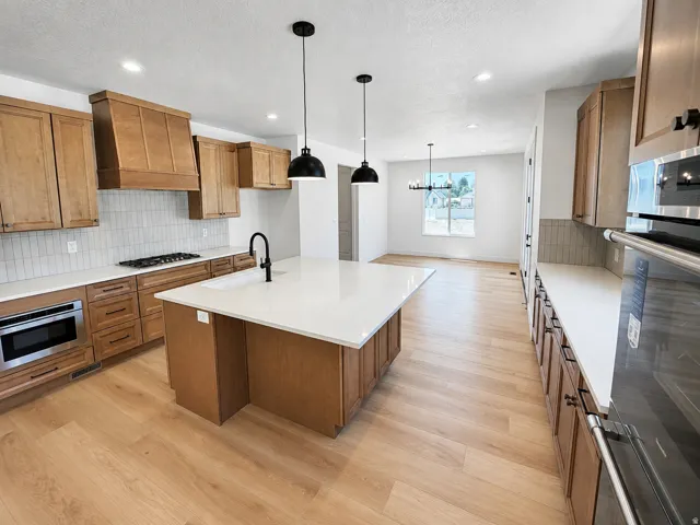 Kitchen featuring wood-finish cabinetry, light countertops, a center island with sink, and stainless steel appliances
