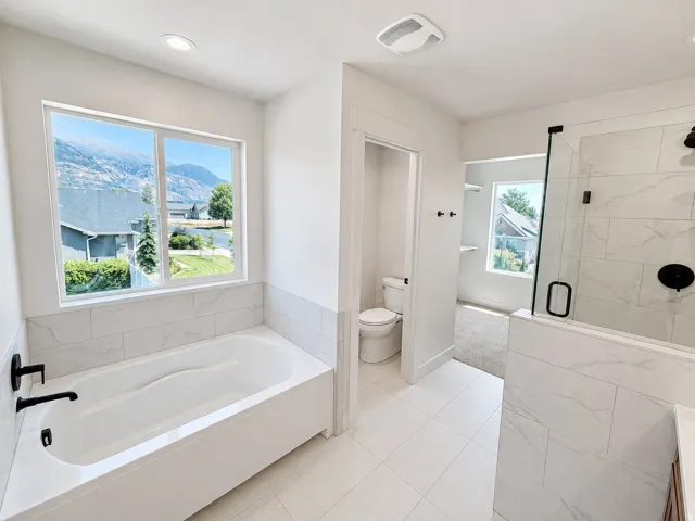 White soaking tub with matte black fixtures, surrounded by white tile wainscoting
