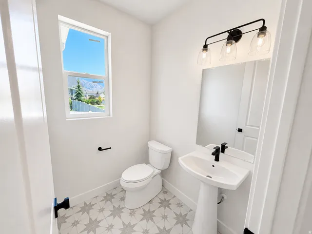 Pedestal sink with a matte black faucet, wall-mounted mirror, and decorative tiled flooring