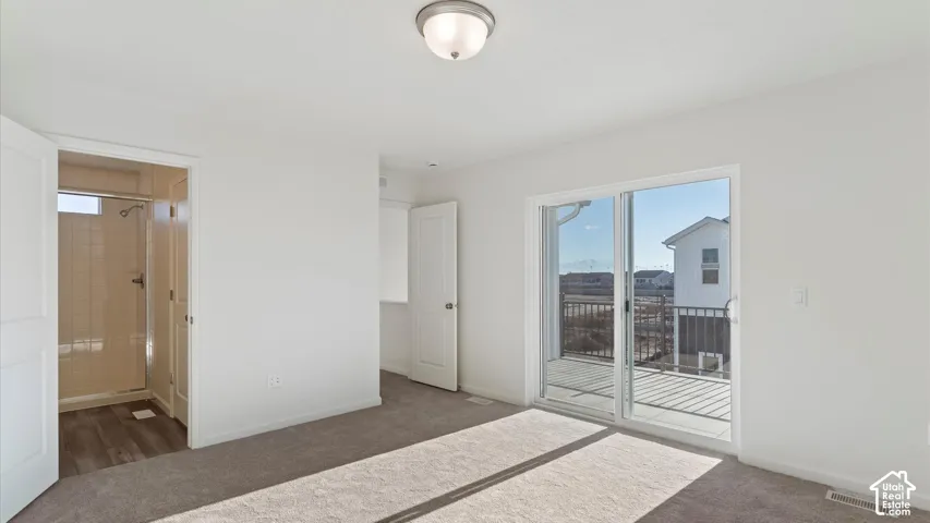Sliding glass door to an exterior balcony with black metal railing, overhead light fixture, and plush carpet