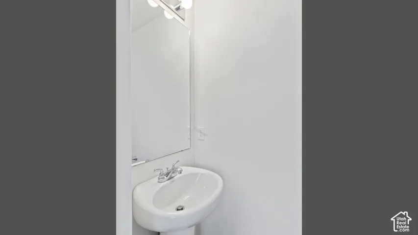 Pedestal sink with chrome faucet, wall-mounted mirror, and vanity lighting