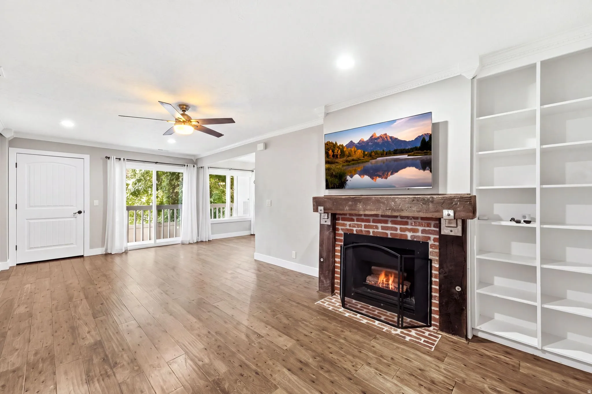 Wood-finish flooring, recessed lighting, ceiling fan, brick fireplace with wood mantel, and built-in shelving