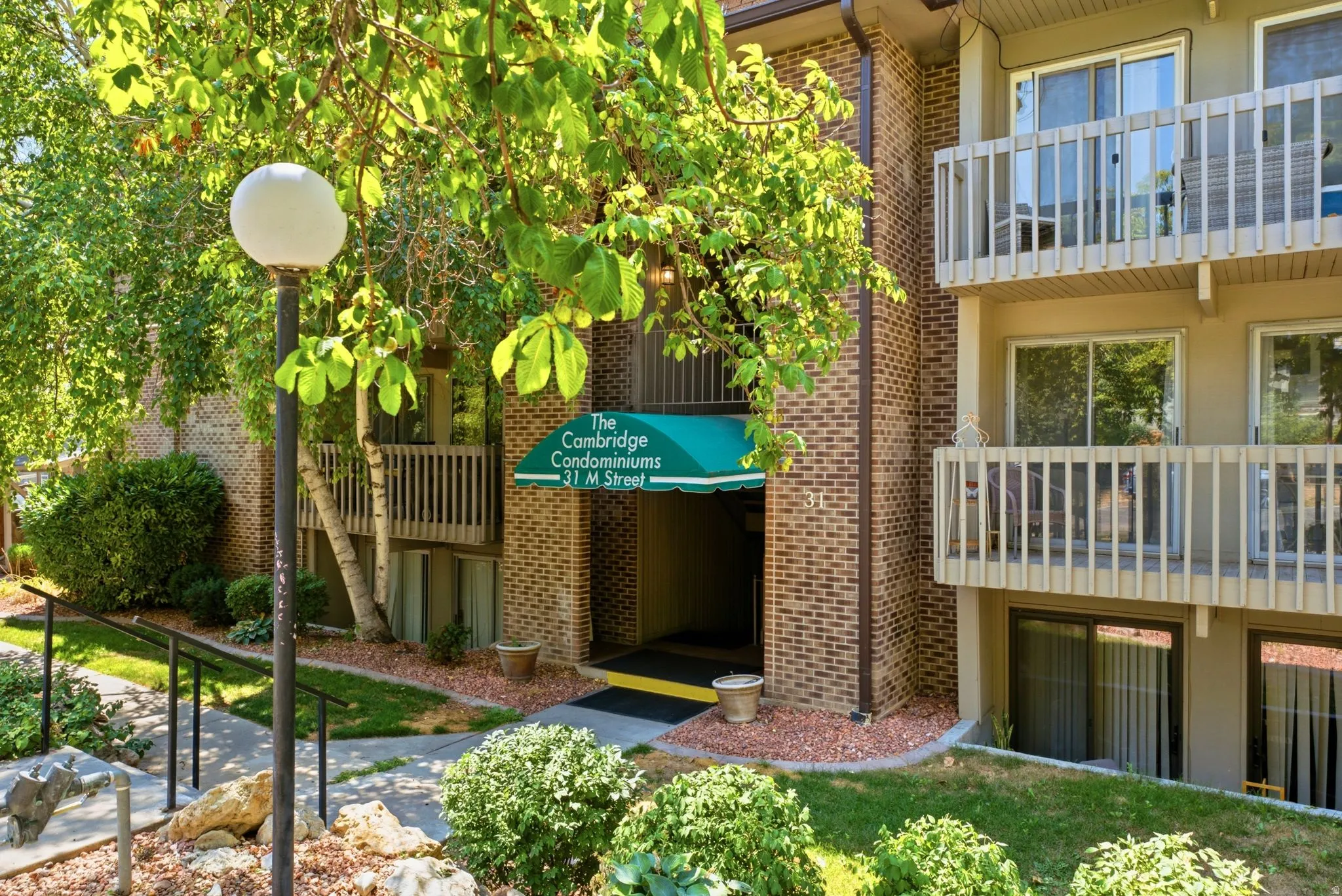 Brick exterior with multiple balconies, a covered entrance, and mature landscaping