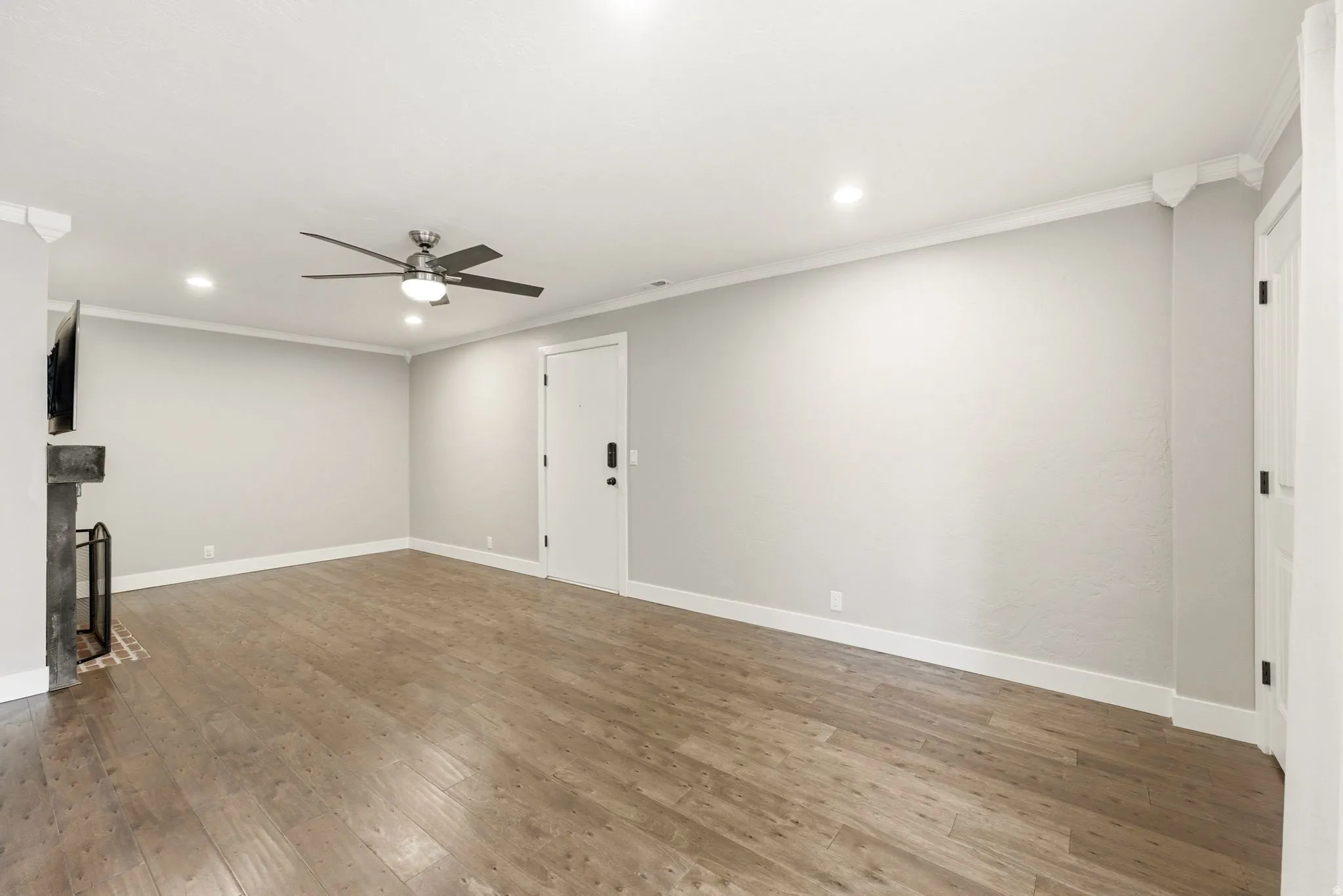 Spacious room with wood-finish flooring, recessed lighting, ceiling fan, and a fireplace with brick hearth