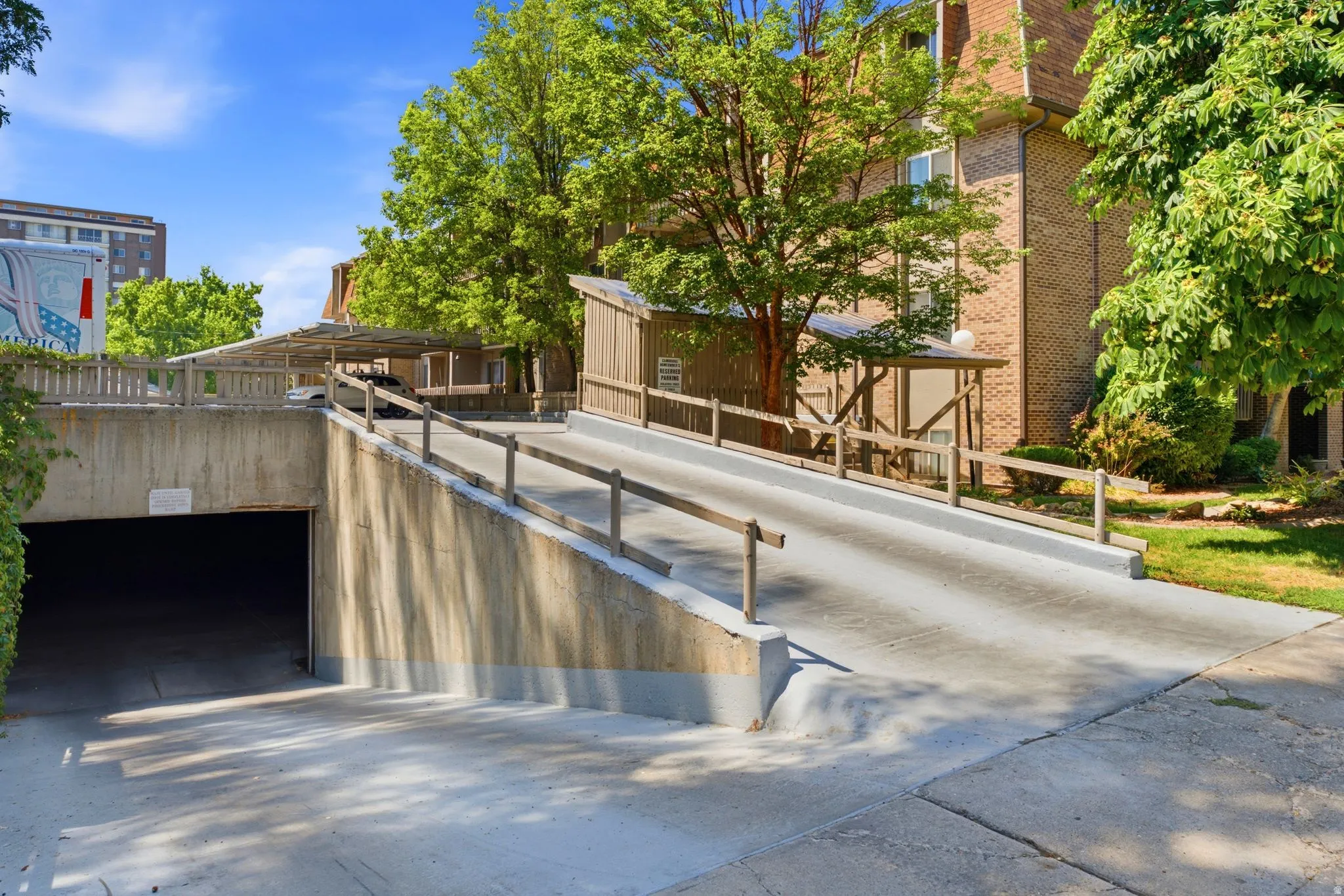 Concrete access ramp with wooden railing, leading to a covered parking area and an underground garage entrance