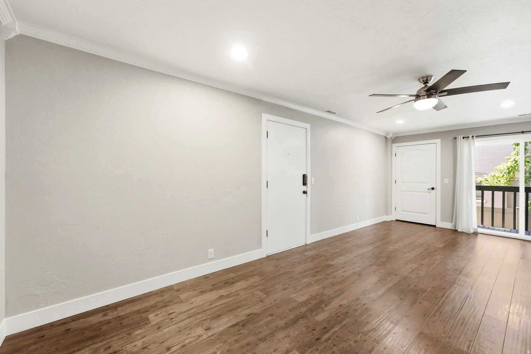 Wood-finish flooring, recessed lighting, ceiling fan with light fixture, white trim, and a balcony with black railings