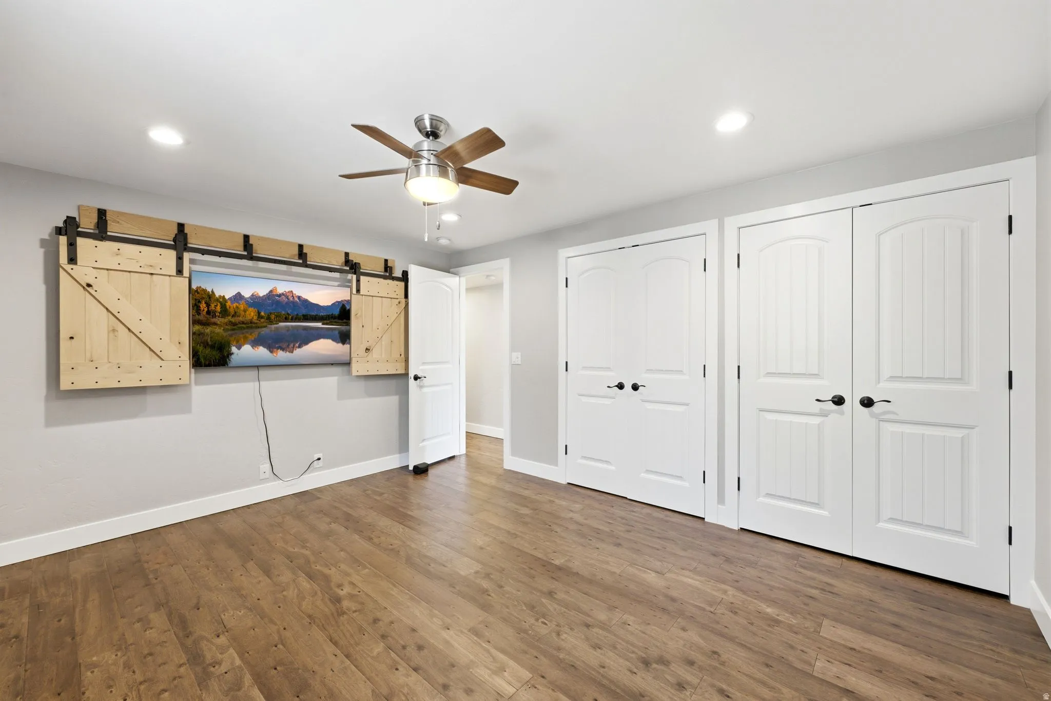 Wood-finish flooring, recessed lighting, ceiling fan with light fixture, decorative barn door media cover, and arched panel doors