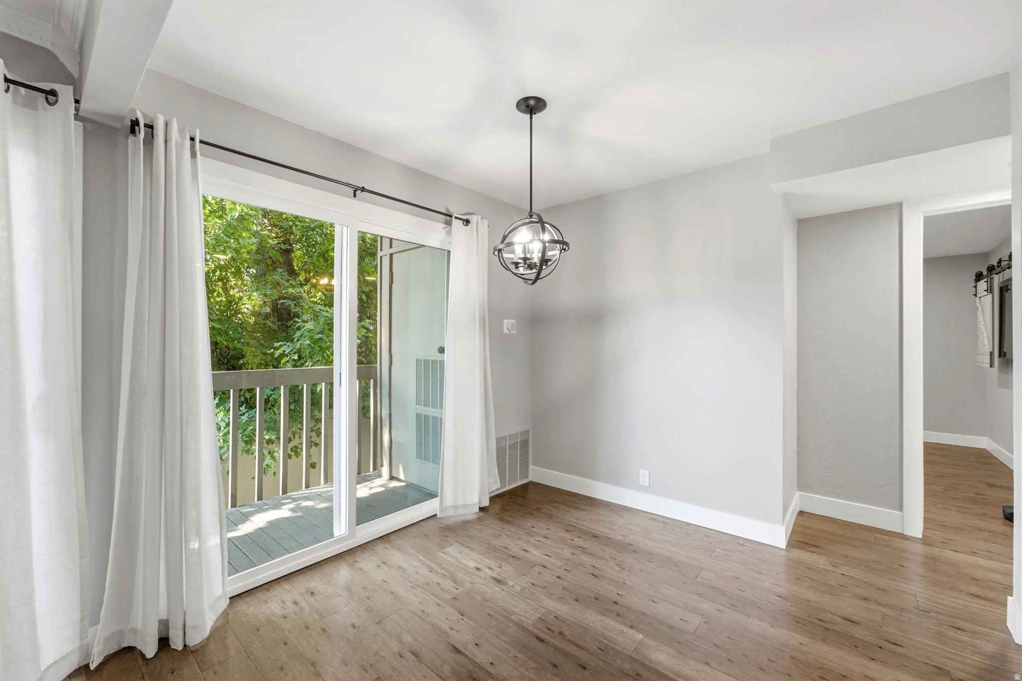 Sliding glass doors opening to an exterior balcony, wood-finish flooring, and a contemporary spherical chandelier