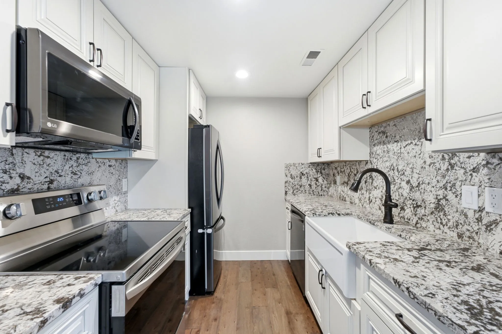 White shaker-style cabinetry, granite countertops, wood-finish flooring, stainless steel appliances, and a farmhouse sink
