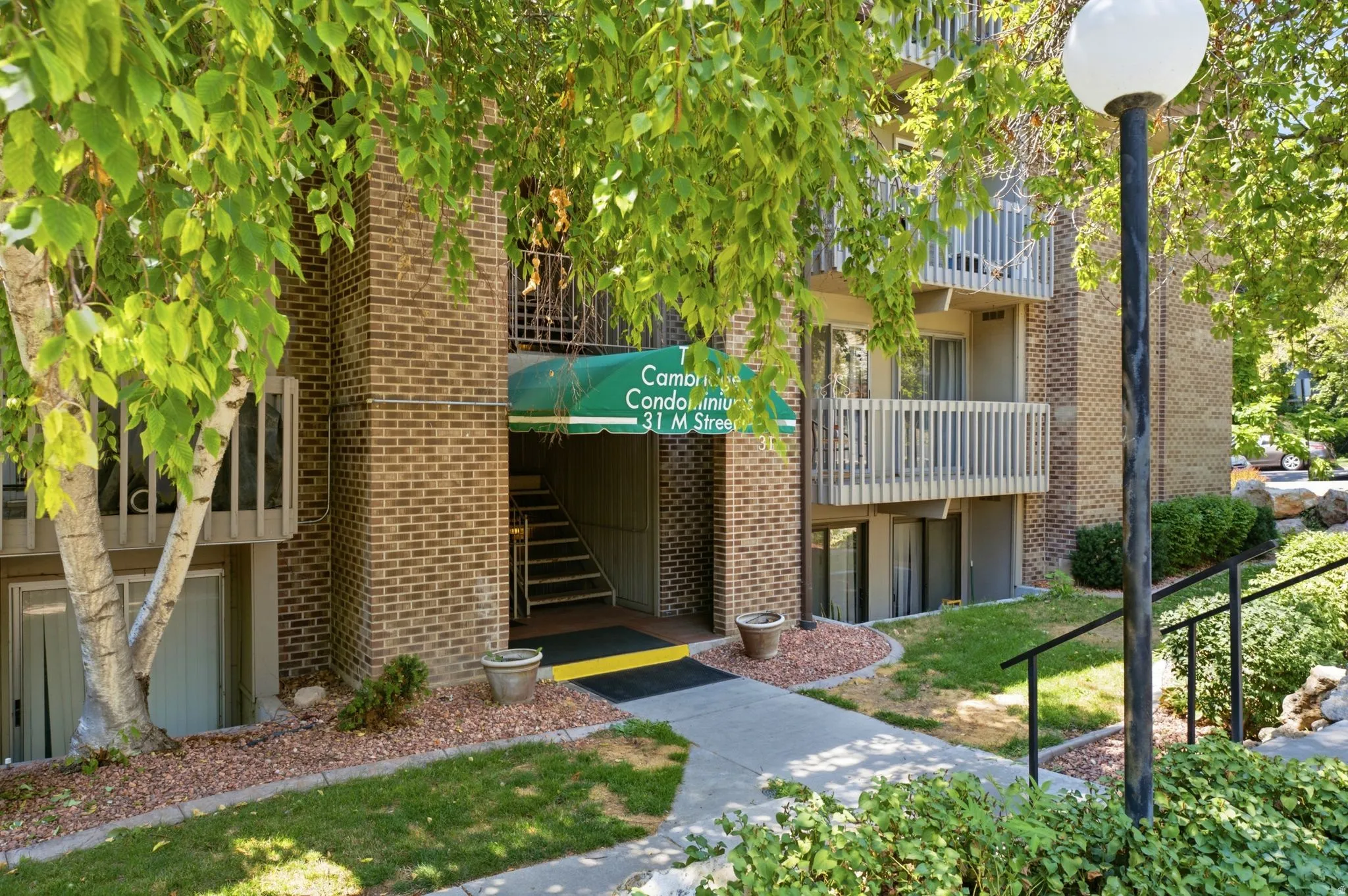 Brick facade with multiple levels of balconies, green awning, concrete pathways, and mature trees