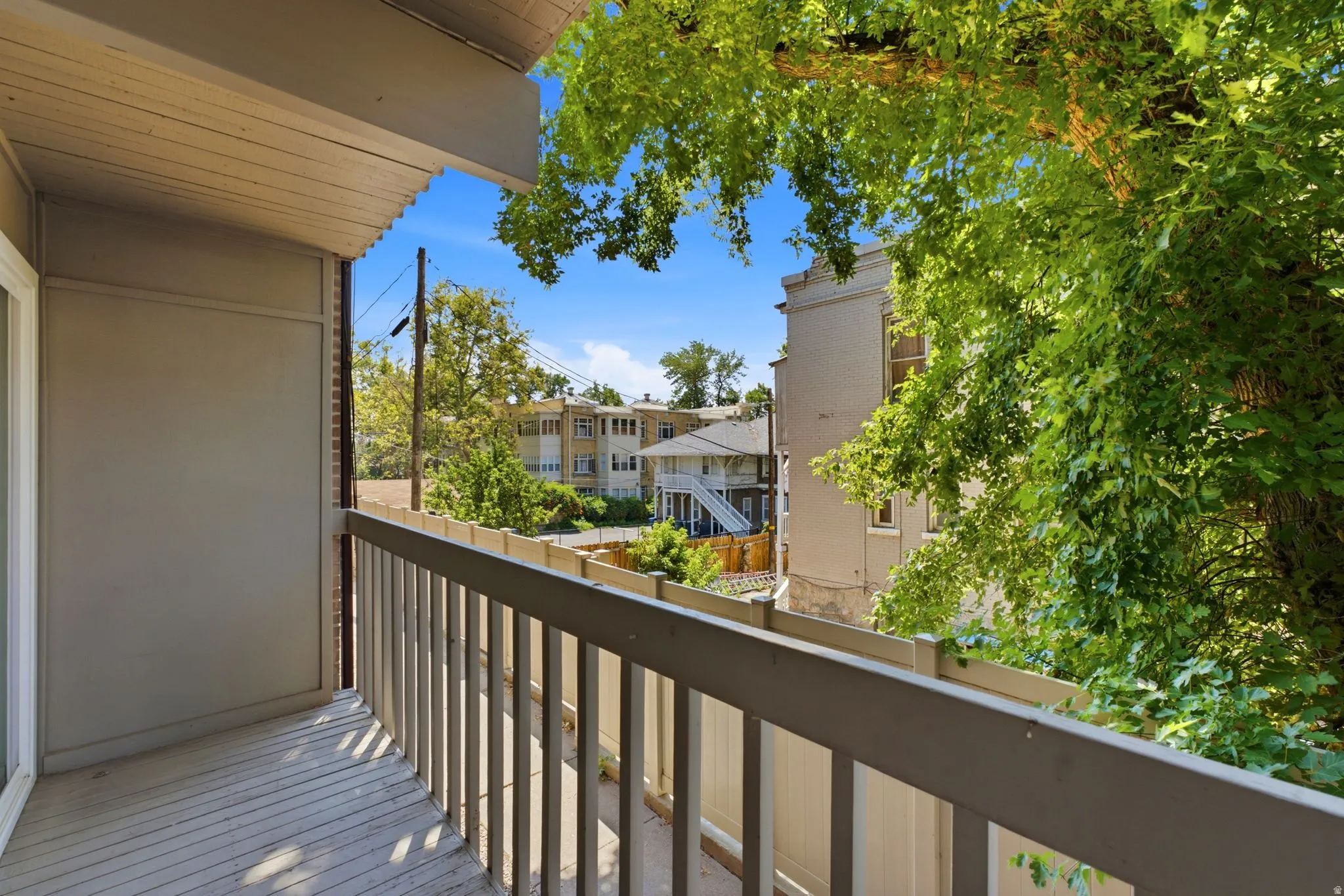 Balcony with wooden railing and slatted decking, featuring an exterior sliding glass door and an overhead soffit